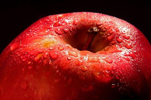 Close up of fresh, juicy, red apple with glistening dew, water drops isolated against plain, black background.