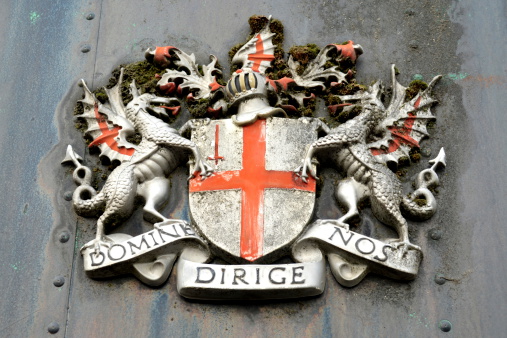 A dirty City of London emblem with dragons and cross of St. George above latin phrase, Domine Dirige Nos, meaning 'Lord DirectUs.'