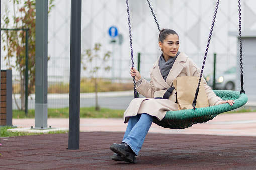 Beautiful young woman sitting on a swing outdoors in city.