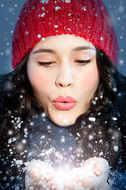 Beautiful young woman blowing snow in hands.