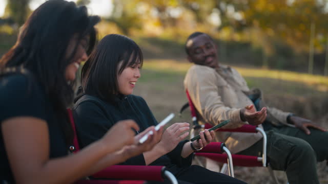Three multi-ethnic friends sitting on camping chairs and enjoying talking with each other in nature in camping site