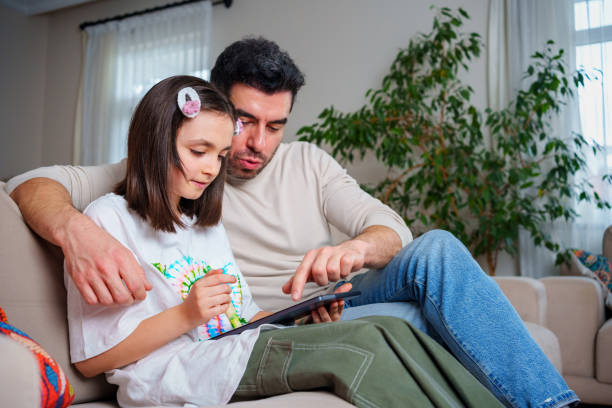 ojciec i nastoletnia córka korzystają razem z tabletem bezprzewodowym podczas relaksu w domu - homework teenager mobile phone school zdjęcia i obrazy z banku zdjęć