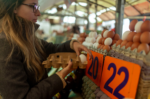 An woman chooses eggs and arranges them in a cardboard egg box while shopping at a street market