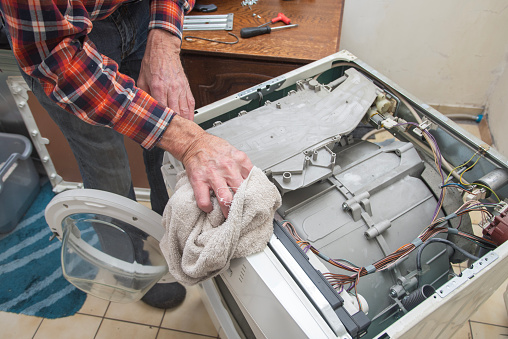 man is a jack of all trades, he removed the lid of the washing machine and wipes the dust inside with a cloth before a thorough inspection and repair, high quality photo