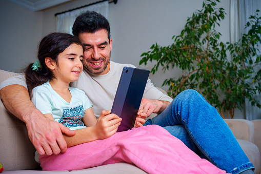 father and  daughter using a wireless tablet together while relaxing at home