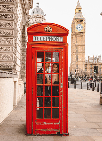 Portrait of a beautiful and happy young couple as they embark on a romantic getaway to the heart of London. Captured inside the iconic red telephone box, they share sweet embraces and kisses, creating cherished moments of love. This image beautifully encapsulates the essence of a romantic vacation or Valentine's Day celebration in the charming city of London.\nRomantic couple, London getaway, red telephone booth, love in the city, travel romance, vacation bliss, Valentine's Day celebration, iconic landmarks, romantic moments, travel photography