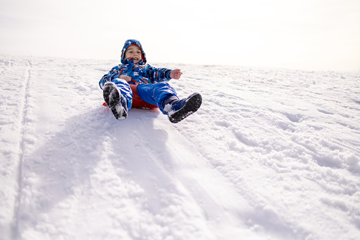 Caucasian boy sledding with sled on the hill, during a winter day on the mountain