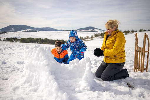 Caucasian family, mother with her two sons, making the fort from the snowball, during their winter vacation on the mountain