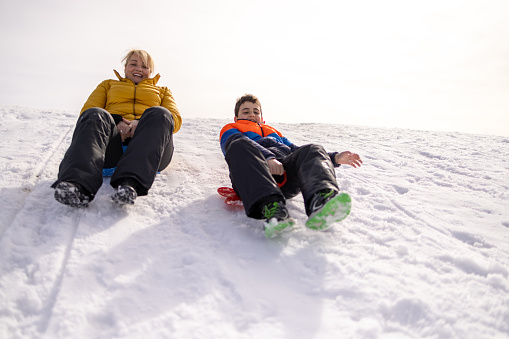 Caucasian boy and his mother sledding with sled on the hill, during a winter day on the mountain