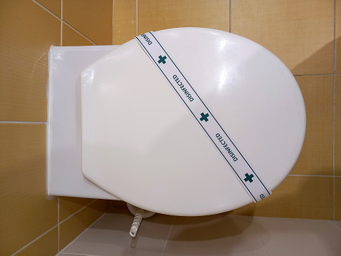 Top view of white toilet seat in toilet. There is a DISINFECTED strip on it. An example of the decor and interior of a hotel bathroom or toilet
