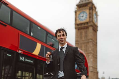 Capturing the essence of a modern businessman's journey, this image features a young and handsome man in a sharp black suit and tie, flashing a confident smile against the iconic backdrop of Big Ben or Elizabeth Tower on Westminster Bridge in London, United Kingdom. The dynamic scene is completed by the passing of a classic red double-decker London bus, adding a touch of urban charm to the business trip.
Business Traveler, Young Man, London Trip, Stylish Businessman, Big Ben, Cityscape, Iconic Landmarks, London Bus, Urban Elegance, Professional Style, Business Fashion, Modern Entrepreneur