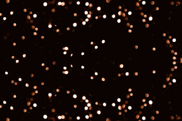 Blurry garland lights on a dark background. Festive Christmas and New Year background. Soft focus. Image toned in color of the year 2024 - Peach Fuzz stock photo