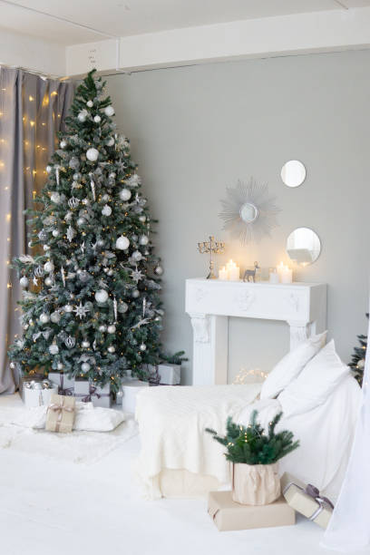 istock Bright interior with a false fireplace decorated for Christmas. Christmas trees with garlands, balloons and lights. 1858007548