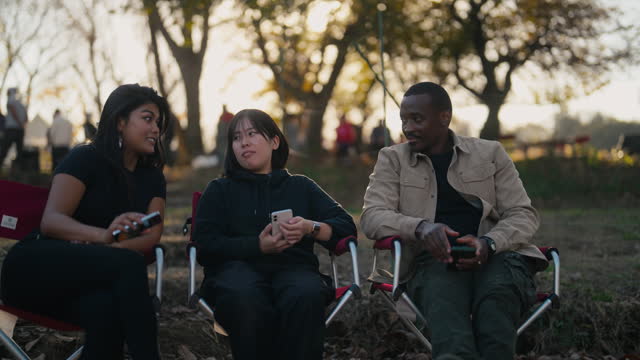 Three multi-ethnic friends sitting on camping chairs and enjoying talking with each other in nature in camping site