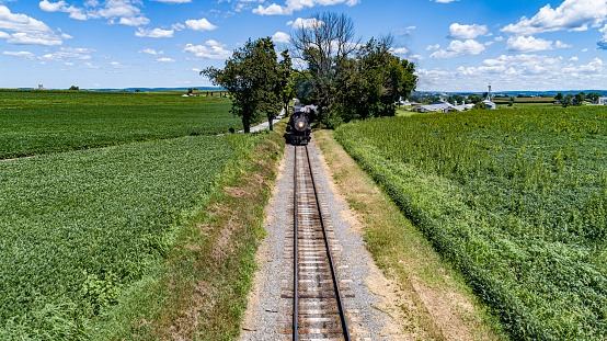 A Head on Drone View of a Steam Passenger Train Approaching on a single Track on a Sunny Summer day
