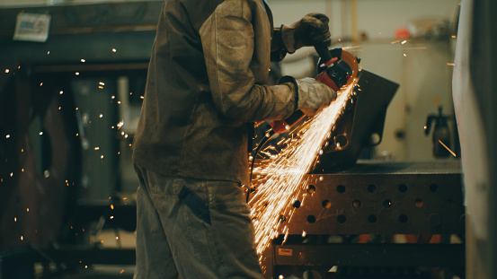 Man using electric grinder tool on a metal with sparks flying around at factory