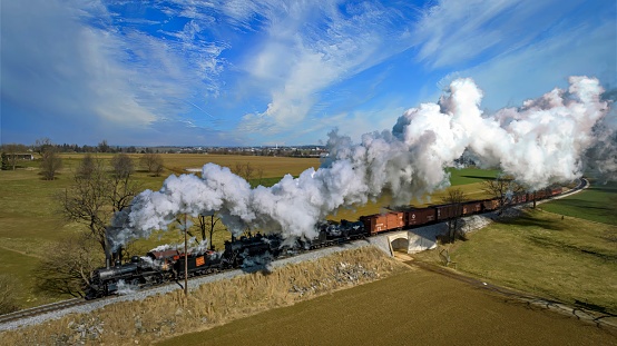 Ronks, Pennsylvania, February 18, 2023 - An Aerial View of a Steam Double-Header Freight , Passenger Combo Train Approaching Blowing Lots of Smoke and Steam on a Sunny Winter's Day
