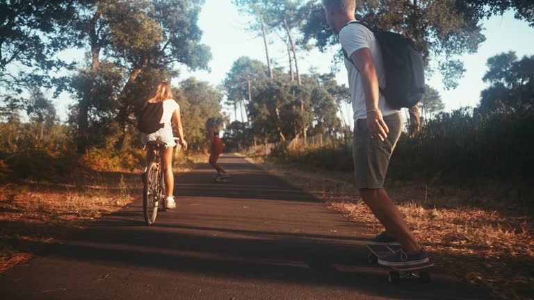 Three friends cycling and skateboarding on forest road