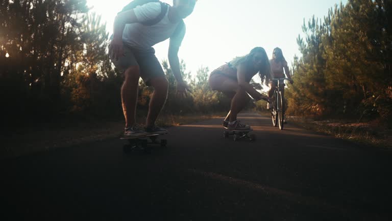 Carefree friends riding bicycle and skateboard on forest road