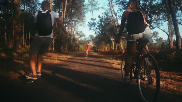 Three friends cycling and skateboarding on forest road