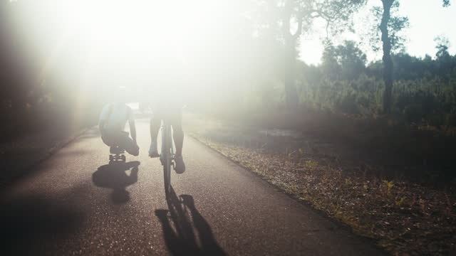 Woman riding bicycle while man is skating in squatting position on forest road