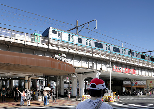 Taito City, Japan - May 24, 2023: A passenger train courses on an elevated track to JR Ueno Station in Taito City. Pedestrians wait at the crosswalk outside the station. Spring afternoon in the Tokyo Metropolis.
