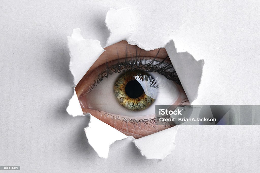 Looking through a hole in white paper Womans eye peeking through a hole in white paper Peephole Stock Photo