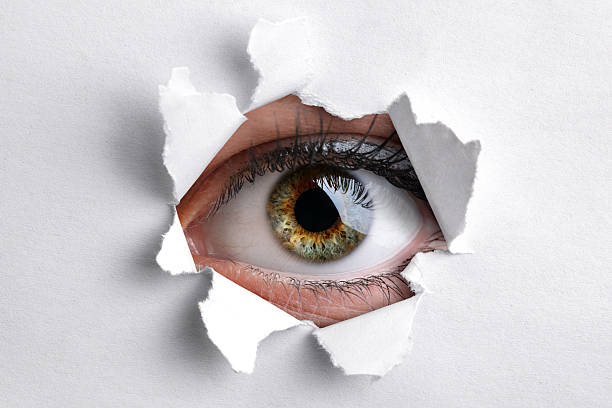 Looking through a hole in white paper Womans eye peeking through a hole in white paper big brother orwellian concept photos stock pictures, royalty-free photos & images