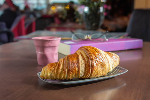 Fresh crispy croissant and coffee cup on a table top inside a cafe