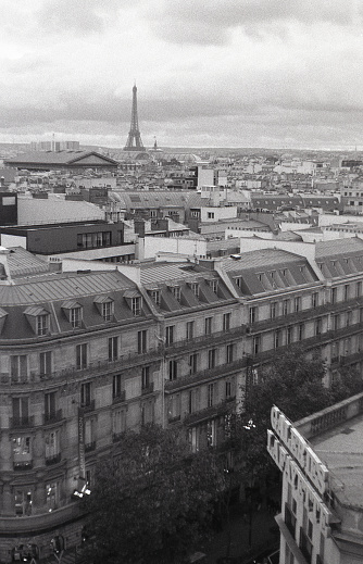 35mm black and white film scan depicting the cityscape of Paris, the elegant capital of France seen from the famous Laffayette Galleries. The iconic Eiffel Tower stands in the background and oversees the rooftops.