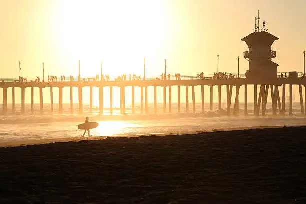 Sunset at Huntington Beach pier in California with a silhouette of a surfer.