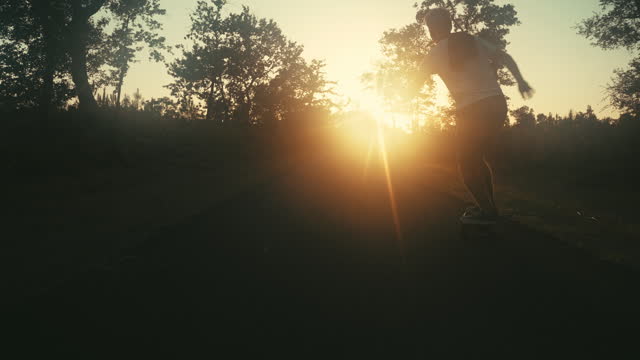 Silhouette of man riding skateboard on forest road