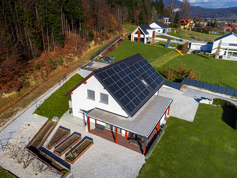 Aerial view of a modern house with solar panels on the roof, surrounded by greenery in a residential area.