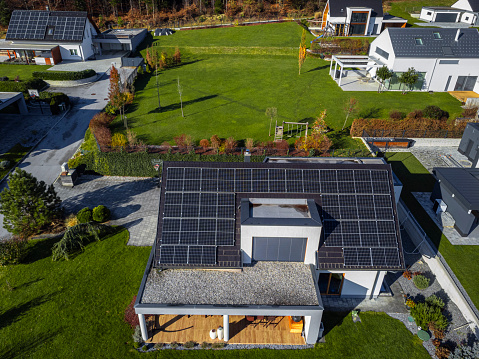 Aerial view of a modern house with solar panels on the roof, surrounded by a green lawns and other homes with solar panels, showcasing sustainable energy solutions