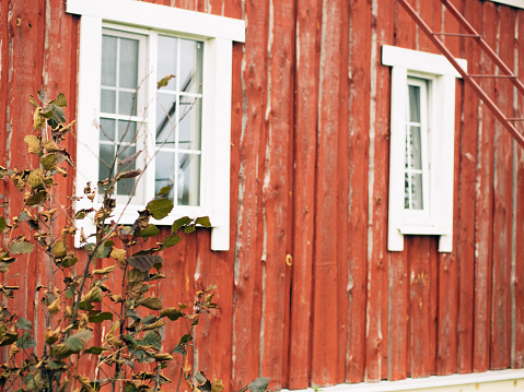 Red rustic wooden barn facade and stone foundation with white window