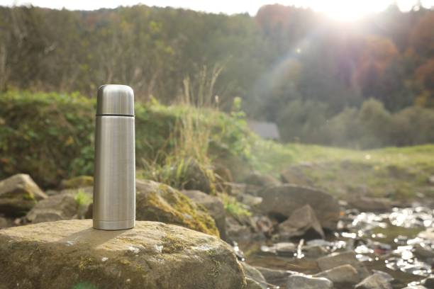 istock Metallic thermos on stone near river, space for text 1858198338