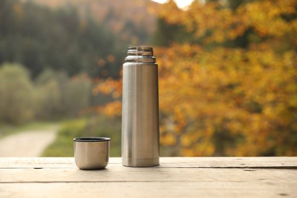 istock Metallic thermos and cup lid on wooden table outdoors, space for text 1858198847