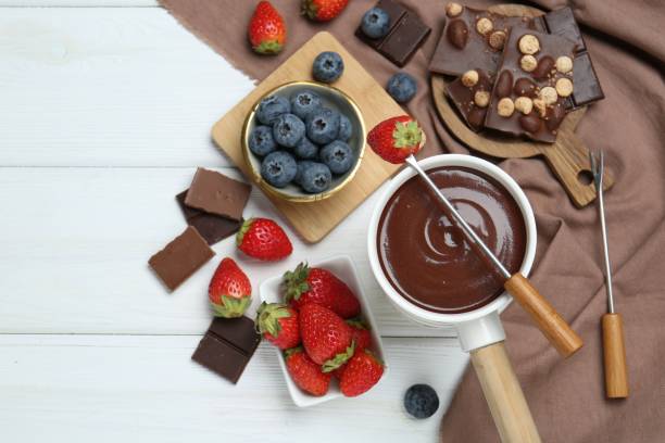 istock Fondue pot with chocolate, different berries and forks on white wooden table, flat lay. Space for text 1858216890
