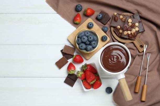 istock Fondue pot with chocolate, different berries and forks on white wooden table, flat lay. Space for text 1858217403
