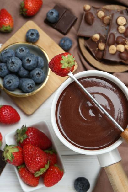 istock Fondue pot with chocolate, different berries and fork on white wooden table, flat lay 1858217928