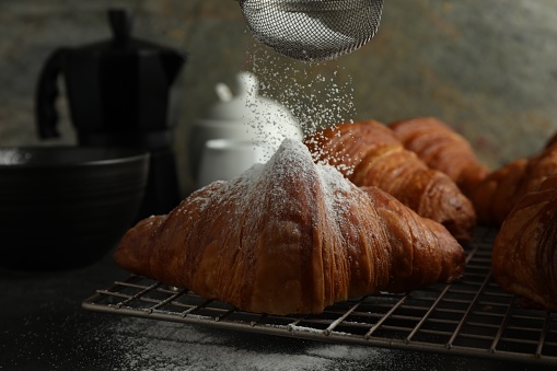 Dusting powdered sugar onto delicious fresh croissants at grey table