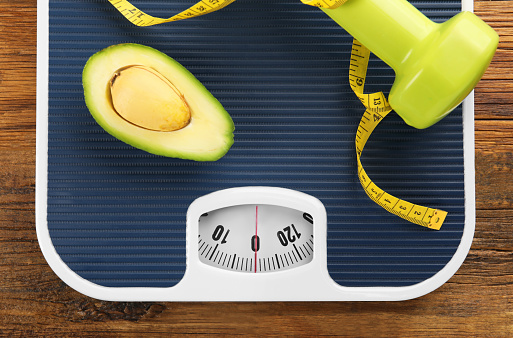 Healthy diet. Scale, avocado, measuring tape and dumbbell on wooden table, top view