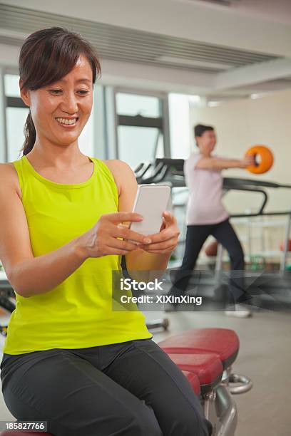 Matura Donna Utilizzando Il Suo Telefono Cellulare In Palestra - Fotografie stock e altre immagini di 40-44 anni