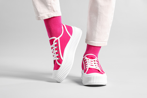 Woman in stylish bright pink socks, sneakers and pants on light grey background, closeup