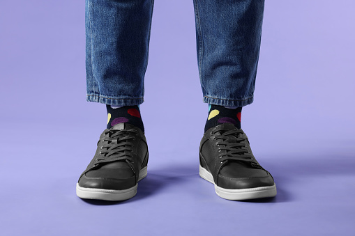Man in stylish colorful socks, sneakers and jeans on violet background, closeup