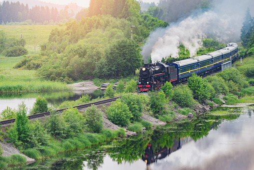 Retro steam train moves along the lake at sunrise.