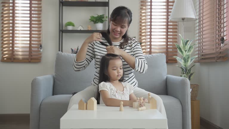 Mother brushing her daughter's hair at home in the living room