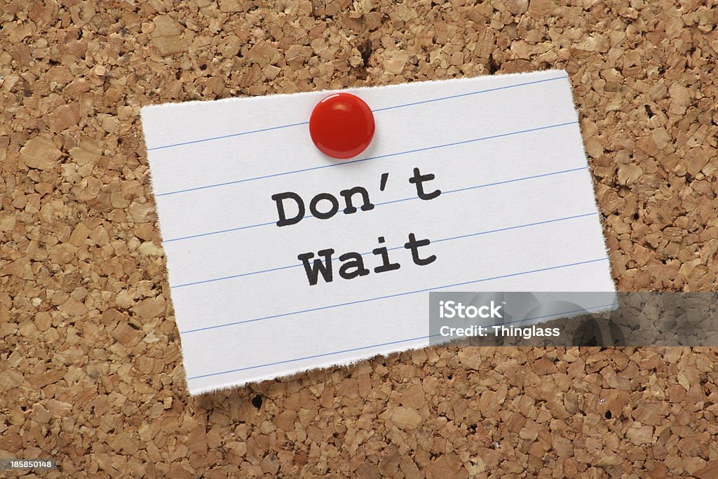 Don't Wait typed on notepaper tacked to a bulletin board The phrase Don't Wait typed on a scrap of lined paper and pinned to a cork notice board. Waiting Stock Photo