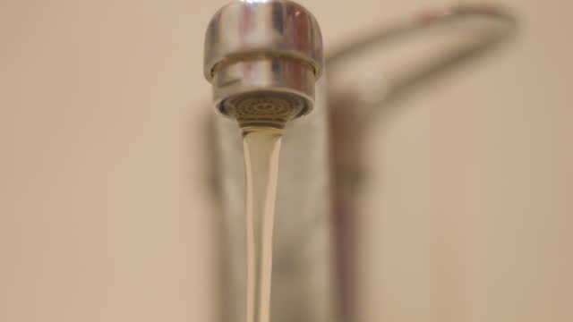 close-up of a hand opening a faucet from which dirty yellow water flows. problems with the plumbing, dirty tap water in the apartment. environmental problems