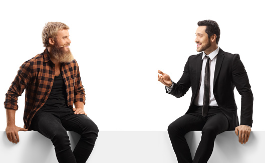 Businessman seated on a white panel talking to a guy with beard and moustaches isolated on white background